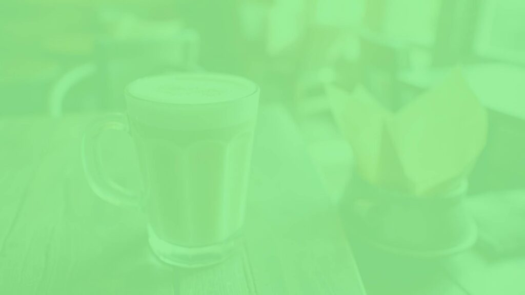 A creamy vanilla latte in a clear glass cup, topped with frothy steamed milk and a light dusting of vanilla, set on a rustic wooden table with soft morning light, cozy and inviting atmosphere.