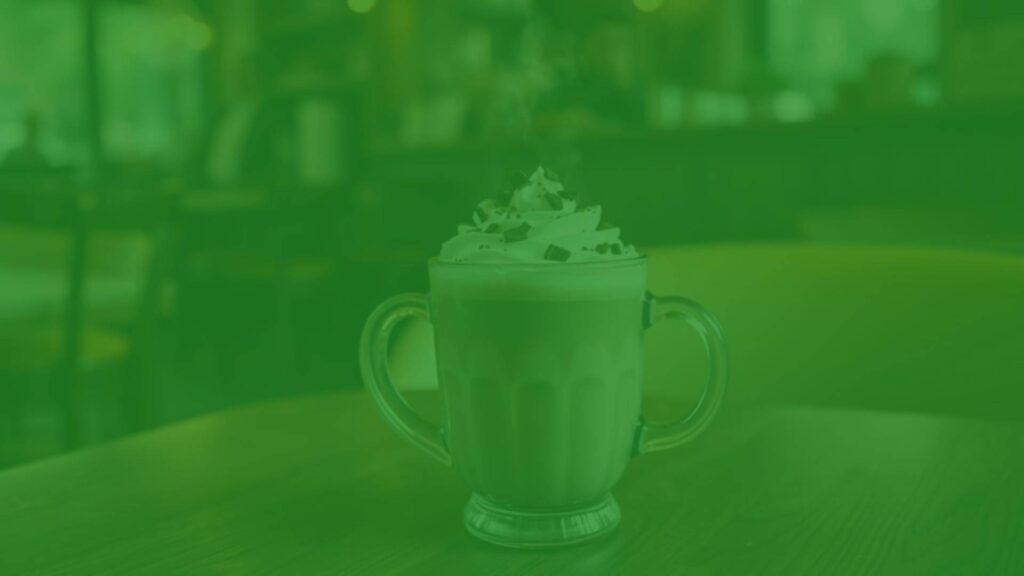 A steaming chocolate latte in a glass mug, topped with whipped cream and chocolate shavings, placed on a wooden table in a cozy cafe setting, warm and inviting lighting, hyperrealistic.