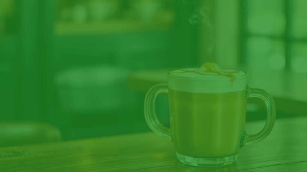 A steaming caramel latte in a glass mug, golden color, topped with foam and caramel drizzle, on a rustic wooden table, cozy cafe ambiance, realistic.