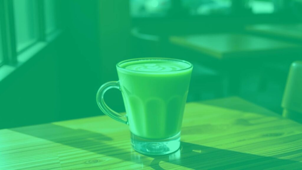 A vibrant matcha latte in a glass cup, emerald green with creamy milk swirls, placed on a wooden café table with natural lighting, photorealistic.